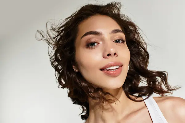 A young woman with elegant curls and beautiful makeup poses confidently in a studio. — Stock Photo