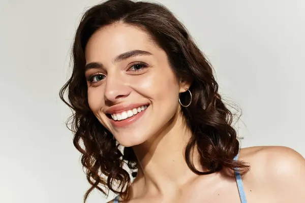 Young woman with gorgeous makeup poses confidently in a grey studio, radiating beauty. — Stock Photo