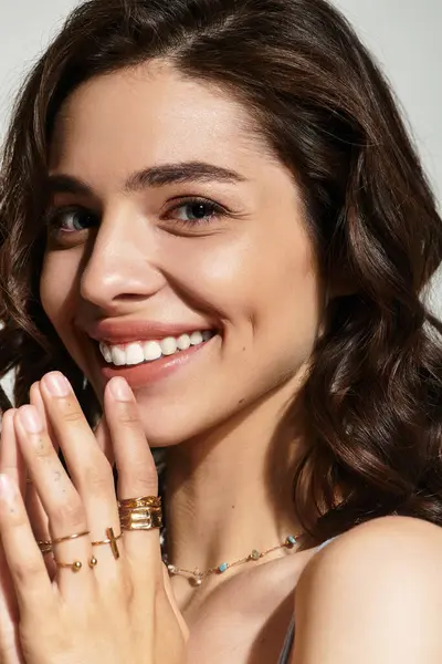 In a studio with a grey backdrop, a young woman poses with a radiant smile, highlighting her makeup. — Stock Photo