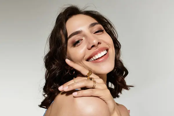 A young woman with beautiful, natural makeup poses confidently in a studio with a grey backdrop. — Stock Photo