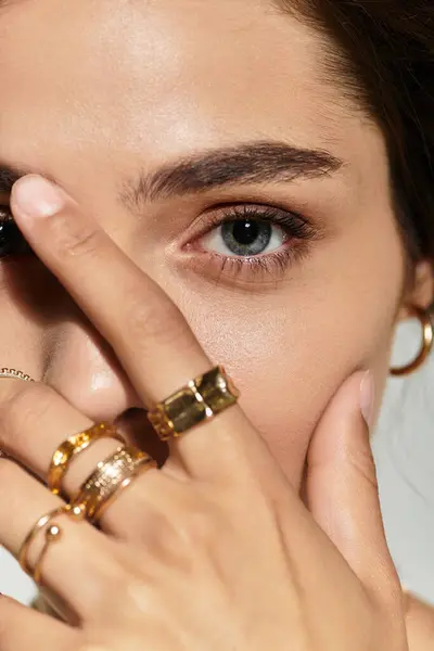 Young woman showcases stunning makeup and stylish rings against a grey backdrop in studio. — Stock Photo