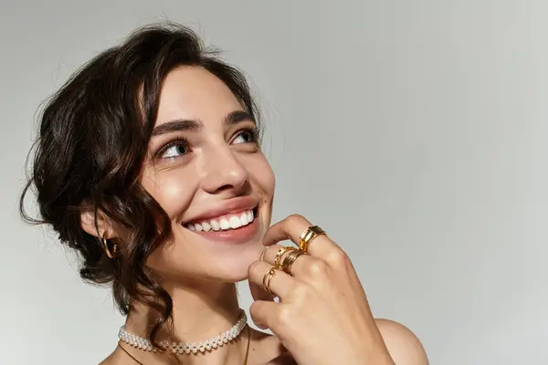 A young woman with stunning makeup smiles brightly, showcasing her style in a softly lit studio. — Stock Photo