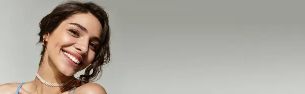 A young woman poses gracefully against a grey backdrop, highlighting her makeup and smile, banner — Stock Photo