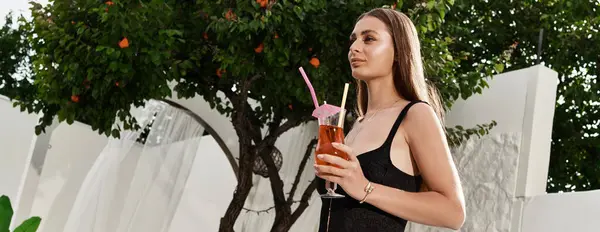 A young beautiful woman holds a colorful drink, soaking up the sun in a lush outdoor garden. — Stock Photo