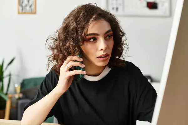 Young woman with curly hair is focused on her work while talking on the phone. — Stock Photo