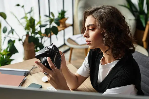 A young woman with curly hair works remotely in her stylish home office, focused on her camera. — Stock Photo