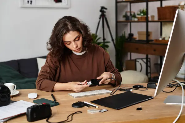A beautiful young woman works on her camera equipment while sitting at a wooden desk in her home. — Stock Photo