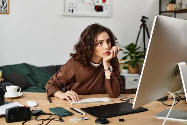 Curly-haired freelancer deeply engaged in work, surrounded by tools in a stylish home office. — Stock Photo