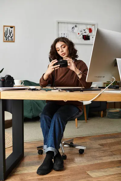 A young woman with curly hair focuses on her camera while working in her stylish home office. — Stock Photo