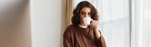 Curly brown-haired woman takes a peaceful break while sipping from her coffee cup at home, banner — Stock Photo