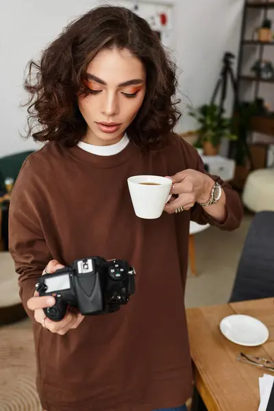 A young woman with curly hair sips her coffee as she reviews her latest photography work at home. — Stock Photo