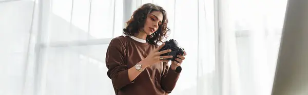 A young woman with curly hair reviews her camera settings while working from home as a photographer, banner — Stock Photo