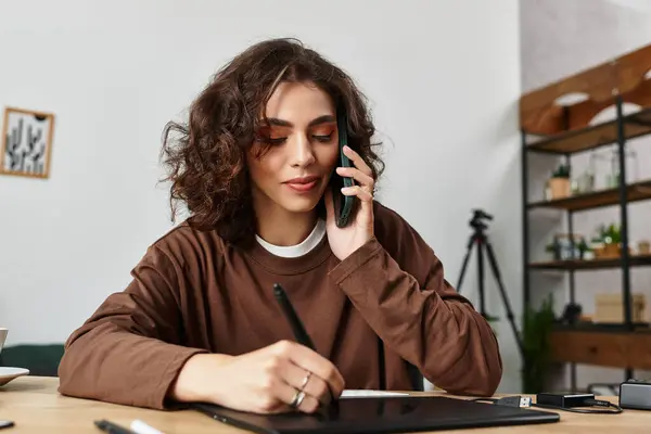 Young woman with curly hair works from home, retouching images and discussing ideas on the phone. — Stock Photo