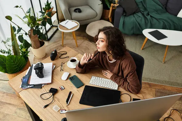 Young woman with curly hair intently edits photos while enjoying a coffee in her home office. — Stock Photo