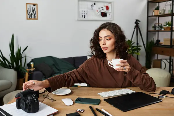 Young woman with curly hair sips coffee while organizing her photography equipment at home. — Stock Photo