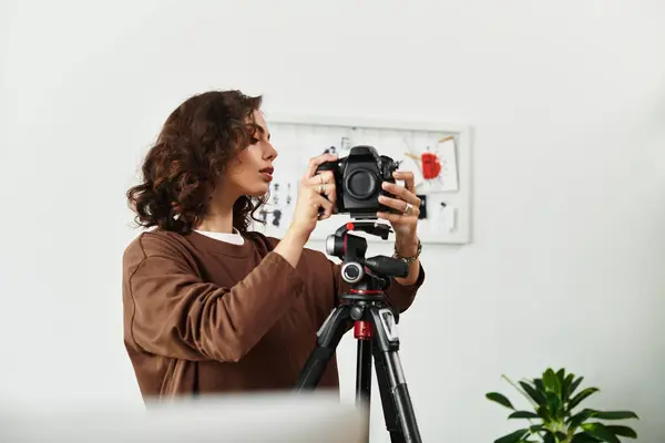 Curly-haired woman focuses intently on her camera while working remotely in a bright space. — Stock Photo