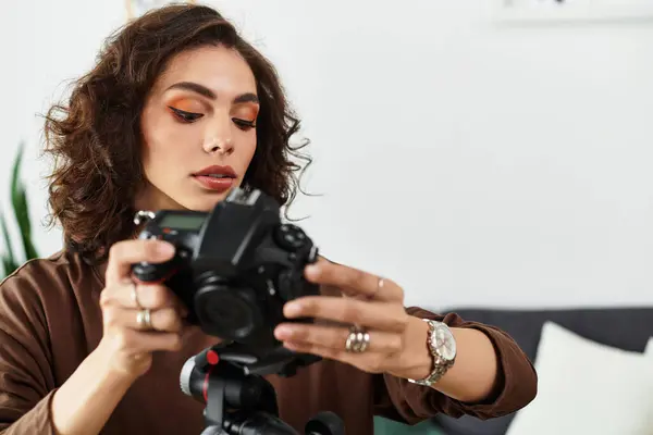 A young woman with curly hair focuses intently on her camera in a cozy home office setup. — Stock Photo