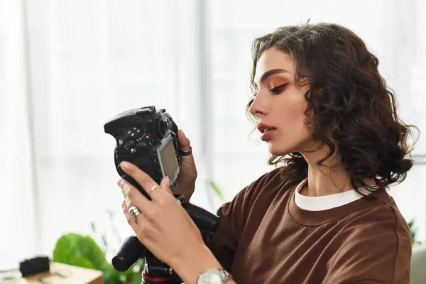 Young woman with curly hair focuses on her camera while working in her home office. — Stock Photo