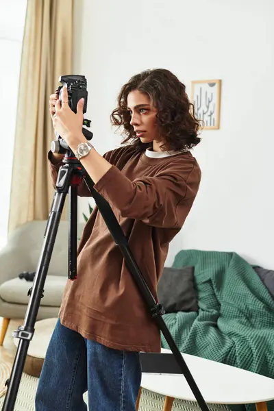 A young woman with curly hair sets up her camera at home, focused on her photography work. — Stock Photo