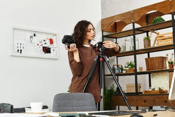 Young woman arranges her camera on a tripod while working from her cozy home office. — Stock Photo