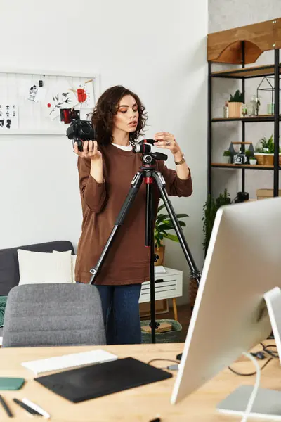 A young woman with curly hair sets up her camera while working in her cozy home office space. — Stock Photo