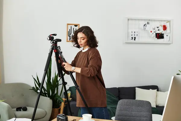 A young woman sets her camera on a tripod in her cozy home workspace, focusing on her craft. — Stock Photo