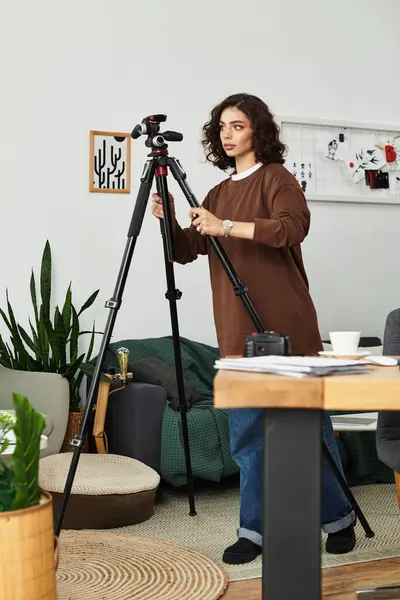 A young woman with curly hair adjusts her camera setup in a bright, stylish home office. — Stock Photo