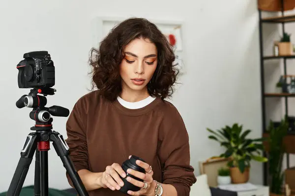 Curly-haired freelancer focuses on her camera equipment in a cozy workspace filled with plants. — Stock Photo