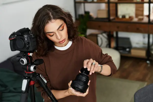 A young woman with curly hair is focused on adjusting her camera lens while working remotely. — Stock Photo