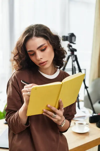 A dedicated young woman with curly hair writes in a notebook amid cozy decor and photography gear. — Stock Photo