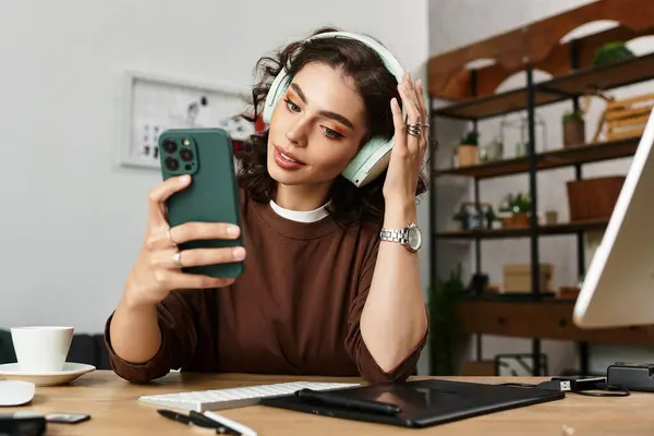 Focused young woman with curly hair edits photos at her home workspace while wearing headphones. — Stock Photo