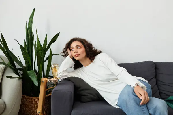 A young woman with curly brown hair relaxes on a couch in her cozy, modern living space. — Stock Photo
