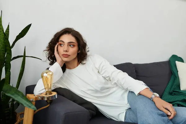 Curly-haired young woman relaxes in a modern apartment, enjoying a peaceful moment in comfort. — Stock Photo
