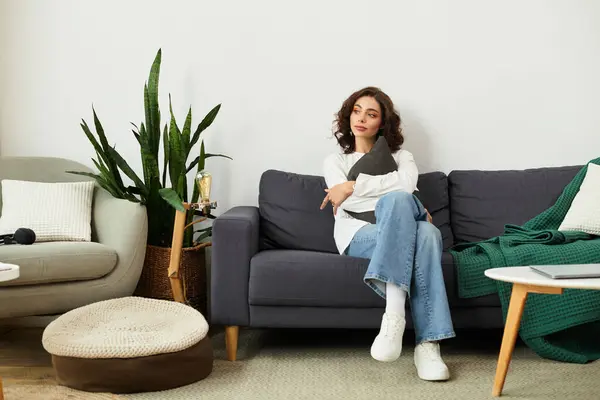 In a stylish apartment, a young woman with curly brown hair sits comfortably on a couch, relaxing. — Stock Photo