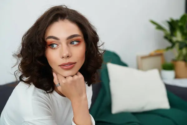 A young woman with curly brown hair relaxes thoughtfully in her modern apartment. — Stock Photo