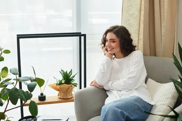 A young woman with curly brown hair smiles thoughtfully in her cozy apartment. — Stock Photo