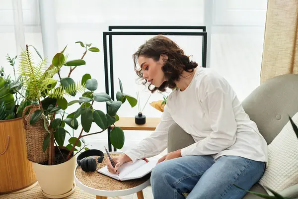 Curly-haired woman journals on a cozy sofa in her stylish, plant-filled apartment. — Stock Photo