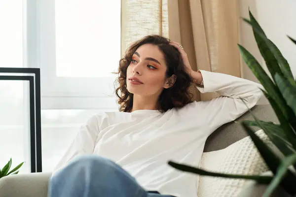 A young woman with curly brown hair relaxes in her modern living space, enjoying peace. — Stock Photo