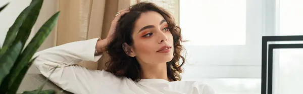 A young woman with curly brown hair enjoys a moment of relaxation in her modern apartment, banner — Stock Photo