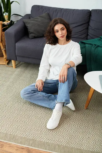 Curly-haired woman in casual attire sits comfortably on the floor, enjoying her serene space. — Stock Photo