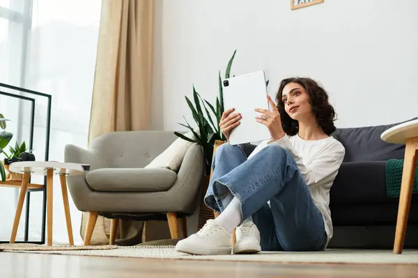 A young woman with curly brown hair sits comfortably on the floor, enjoying her leisure time. — Stock Photo