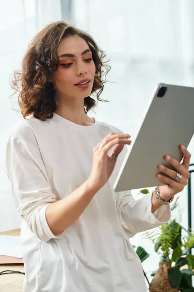 In a modern apartment, a young woman with curly brown hair relaxes as she engages with her tablet. — Stock Photo