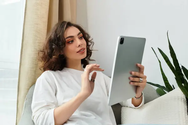 Relaxing in her stylish home, a young woman engages with her tablet, lost in thought. — Stock Photo