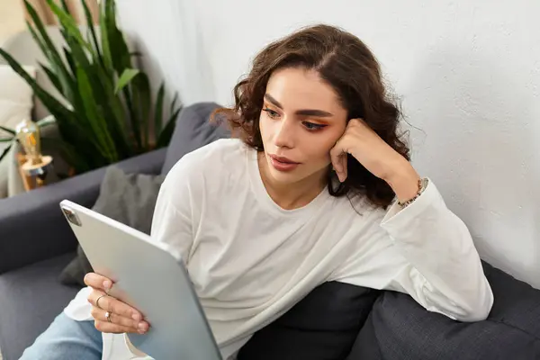 A young woman with curly hair relaxes on a sofa, focused on her tablet in a chic room. — Stock Photo