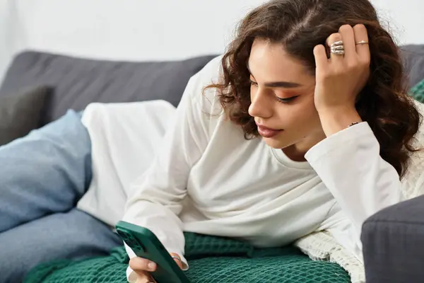 Young woman with curly brown hair enjoys a quiet moment on her phone in her apartment. — Stock Photo