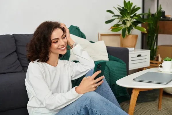 Young woman with curly hair engages with her smartphone while relaxing at home. — Stock Photo