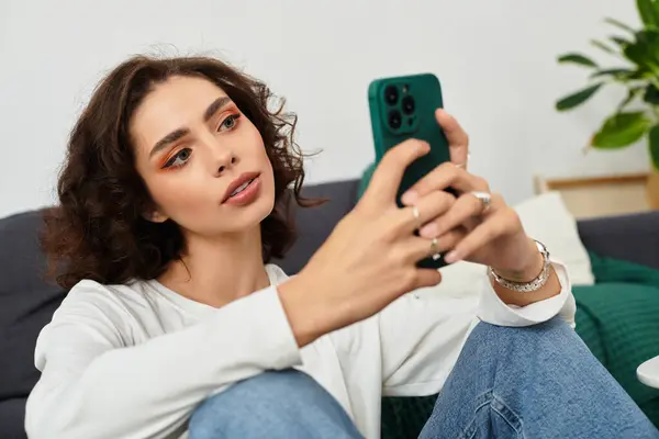 A young woman with curly brown hair relaxes on her phone in a chic living space. — Stock Photo