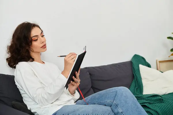 A young woman with curly brown hair journals thoughtfully in her cozy apartment. — Stock Photo