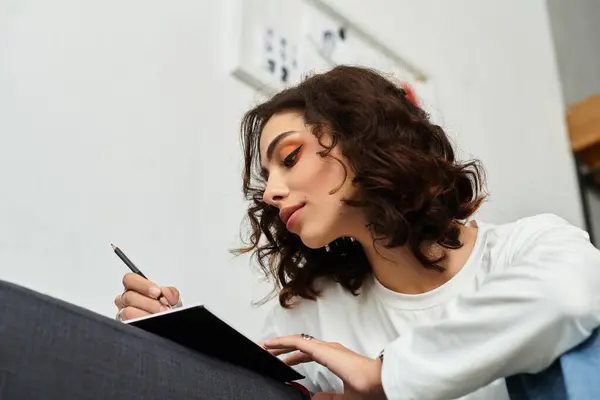 In a stylish apartment, a young woman rests while writing in her notebook, embracing tranquility. — Stock Photo