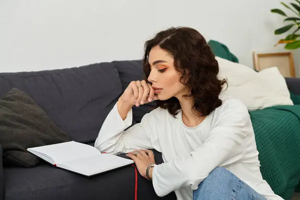 Curly-haired woman relaxes on a couch, reflecting with an open journal in her cozy apartment. — Stock Photo
